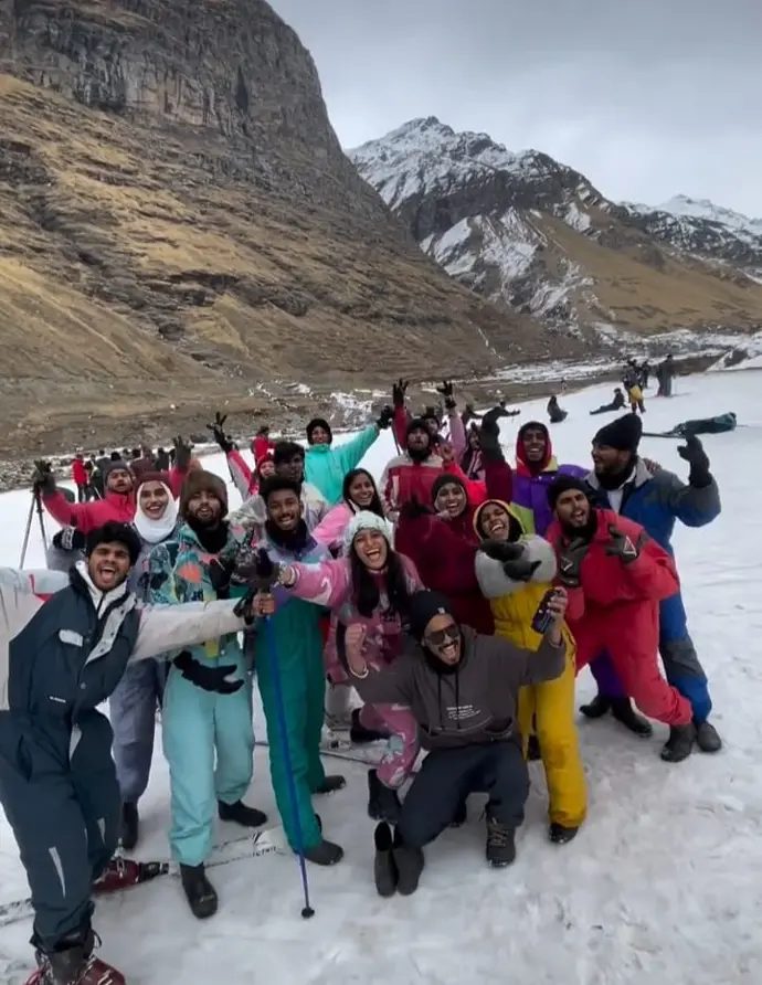 Group of friends laughing and pointing towards the snow-covered peaks of their Kullu Manali trek